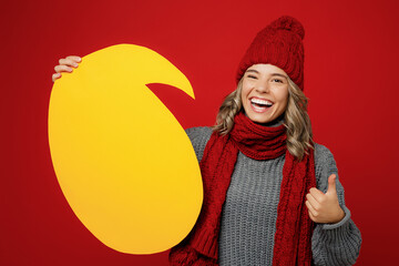Wall Mural - Young fun woman wear grey sweater scarf hat hold yellow empty blank Say cloud, speech bubble isolated on plain red background studio. Healthy lifestyle ill sick disease treatment cold season concept.