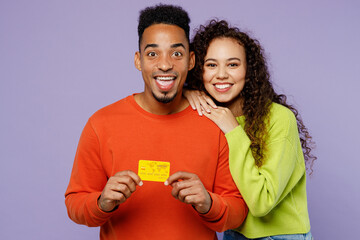 Poster - Young smiling couple two friends family man woman of African American ethnicity wear casual clothes together hold in hand mock up of credit bank card isolated on pastel plain light purple background.