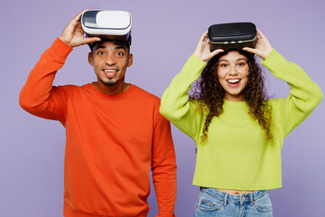 Wall Mural - Young excited surprised couple two friend family man woman of African American ethnicity wear casual clothes together watching in vr headset pc gadget isolated on pastel plain light purple background