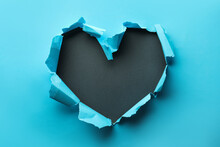 Torn Heart Shaped Hole In Light Blue Paper On Black Background