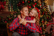 © Liudmila - Girl in red winter dress is posing with her dad in the room with Christmas tree