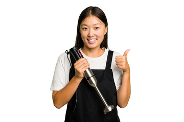 Wall Mural - Young asian cook woman holding a blender isolated smiling and raising thumb up