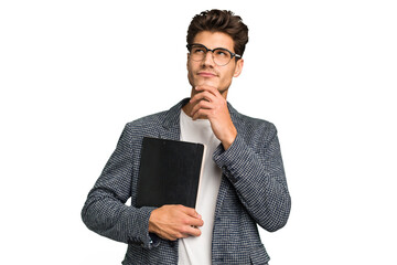 Wall Mural - Young teacher caucasian man holding a book isolated looking sideways with doubtful and skeptical expression.