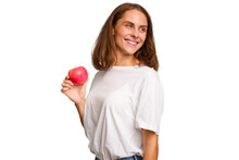 Young Caucasian Woman Holding A Red Apple Isolated Looks Aside Smiling, Cheerful And Pleasant.