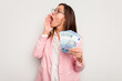© Asier - Business caucasian woman holding banknotes isolated on white background shouting and holding palm near opened mouth.