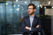 Portrait Of Successful Mature Investor, Senior Businessman Inside Office Looking Towards Window Smiling With Crossed Arms, Man In Glasses And Business Suit.