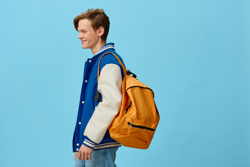 Wall Mural - student with a backpack on his shoulder posing on a blue background