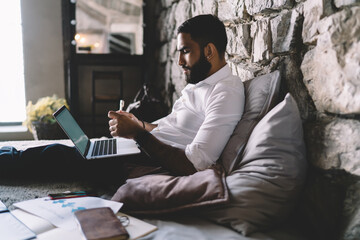 Ethnic man holding pen while working on laptop