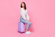 Full body photo of pretty young lady sit baggage wait departure look empty space wear trendy white outfit isolated on pink color background