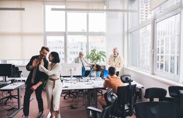 Diverse employees standing in modern office while colleagues discussing project at table