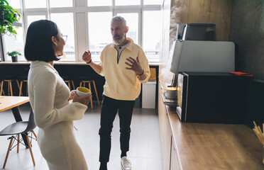 Man and woman standing near office kitchen counter and talking