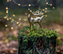 Christmas Golden Deer Toy On The Tree Stump In Forest Close Up.	. Winter Holiday Greeting Card Close Up