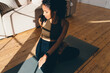 Top view of pretty pregnant african american girl in sports clothes doing twits sitting in lotus posture on floor, under sun rays, practicing prenatal yoga, preparing body for childbirth