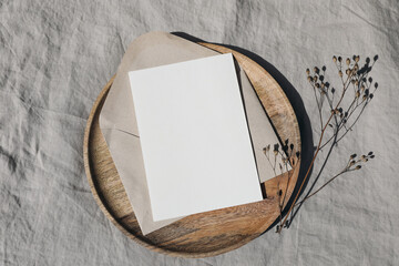 Winter invitation mockup. Blank Christmas greeting card, invitation mock up template with dry plant in sunlight. Wooden plate, tray on linen tablecloth. Festive still life. Flat lay, top view.