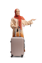 Sticker - Full length portrait of a young woman in ethnic clothes and hijab with a suitcase showing with hand