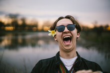 Teenage Boy Laughs With Sunglasses On By Lake At Sunset