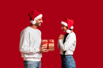 Wall Mural - Christmas Present. Arab Man In Santa Hat Giving Gift To Excited Girlfriend