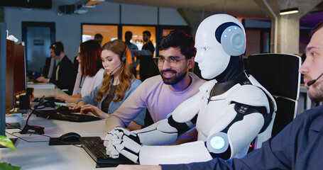 Robot working at computer and men observing. Cyborg typing on keyboard. IT team of future. Futuristic worker. Humanoid work at call center. Support job. Technology concept. Digital transformation