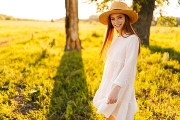 Wall Mural - portrait of charming ginger young woman in straw hat and white dress standing posing on beautiful me