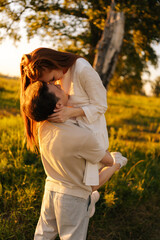 Wall Mural - vertical shot of loving young man holding pretty redhead woman in arms on green meadow in sunny summ