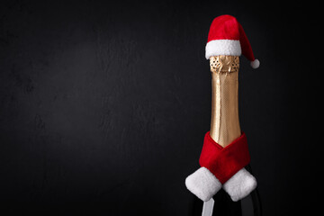 Wall Mural - Champagne bottle wearing christmas hat and red knitting scarf on black background. New Year concept