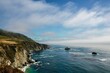 Big Sur's rugged landscape of sea waves crashing the cliffs under a cloudy sky, California