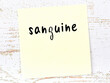 Yellow sticky note on wooden wall with handwritten word sanguine