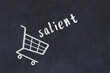 Chalk drawing of shopping cart and word salient on black chalboard. Concept of globalization and mass consuming