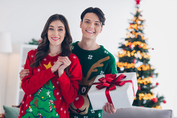 Poster - Photo portrait of two smiling people wear ugly christmas sweaters hold new package giftbox from santa claus atmosphere xmas spirit indoors