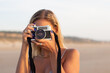 © KAMPUS - Portrait of woman with old-fashioned camera. Female model with fair hair and in casual clothes holding camera on beach. Hobby, travelling concept