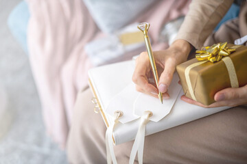 Closeup female hands writing Christmas festive congratulations on card for gift box package