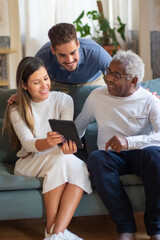 Portrait of aged man and grandchildren using tablet. Happy old man spending week ends with relatives, young guys showing him video in internet on tablet. Senior people and modern technologies concept