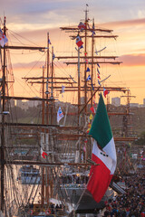 Wall Mural - ROUEN, NORMANDY, FRANCE: Armada 2019 gathering of tall ships on the Seine river, crowds of visitors walk on the dock and visit the ships at sunset, mexican flag in foreground