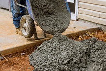 With Help Of Using Wheelbarrow, They Are Making New Concrete Footpath Near House By Pouring Wet Cement Concrete