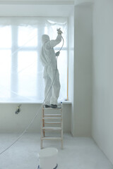 Wall Mural - Decorator painting window slope on ladder indoors, back view