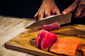 Wall Mural - Close up of Chef cook hands chopping tuna fish for traditional Asian cuisine with Japanese knife. Professional Sushi chef cutting seafood japanese chefs are making tuna fish sashimi. dark tone