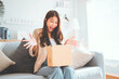 © oatawa - Excited young asian woman unpacking carton box and looking inside, Emotional female surprised by fast delivery service, Happy woman client satisfied with ordered purchase, Online shopping.