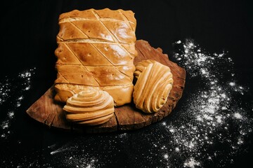 Wall Mural - Top view of a wooden board with sweet puff pastry buns on a black background