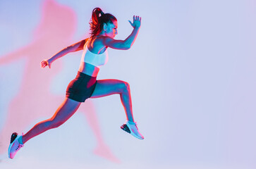 artistic image with colored gel lights of a beautiful fit woman making exercises in the gym with spo