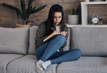 Book, writing and woman on sofa for thinking, journal and creative, brainstorm and notes in a living room. Notebook, planning and girl on couch for diary entry, strategy and vision for future in home