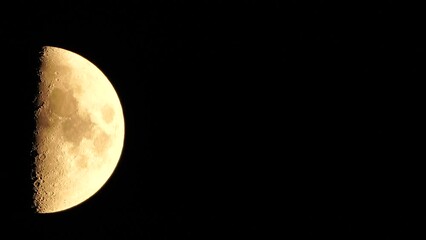 Wall Mural - A glowing golden huge half moon seen from earth through the atmosphere against a starry night sky. A large moon moves across the sky, the moon moving from the left frame to the right.