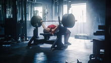Professional Female Athlete Doing Bench Press Workout Using Barbell In A Grunge Hardcore Gym. An Inspiring Bodybuilder Training And Exercising With Heavy Weights In A Deserted Gym. Wide Shot