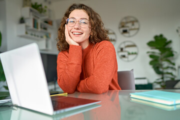 Young happy pretty business woman student sitting at desk at home office with laptop computer looking at camera advertising online learning, remote work, business webinars. Portrait.