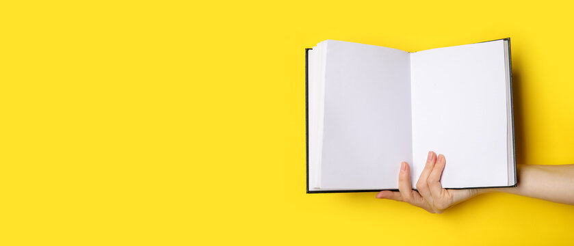 hand holding blank book on yellow background with space for text