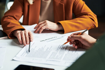 Hand of mature teacher of foreign languages pointing at one of documents while explaining information to student