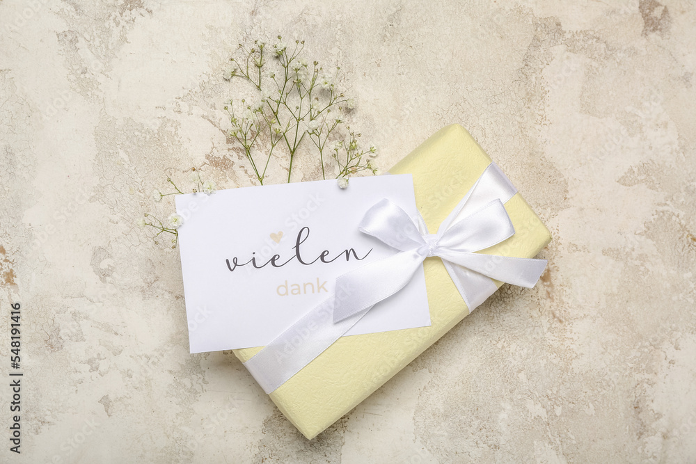 Card with text VIELEN DANK, gift box and flowers on grunge background