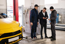 Mechanics And Manager Stand Against Yellow Sport Car Suv In Repair.