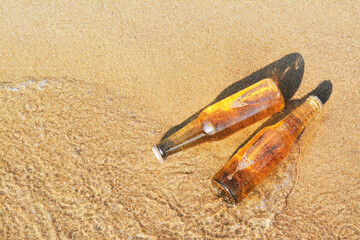 Wall Mural - Bottles of cold beer in water on sandy beach, above view. Space for text