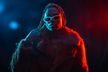 Wall Mural - Woman of black ethnicity with braids with blue and red led lights, wearing a fur coat looking at the camera