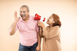 © GAJENDRRA BHATI  - Senior indian woman scream or shouting at man in megaphone isolated on beige background. announce discounts sale. Asian wife tease husband.